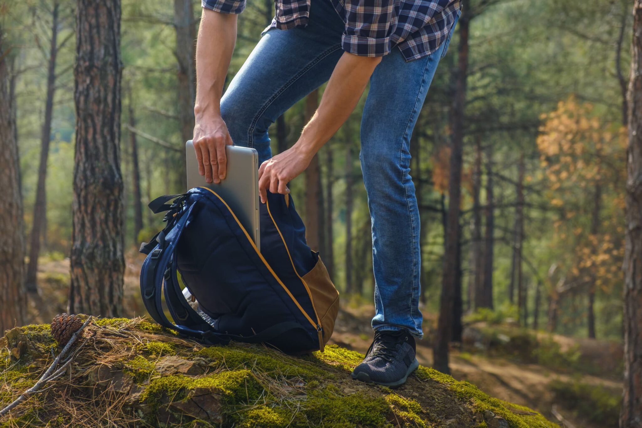 Cropped photography of young man getting laptop from the backpack at the forest